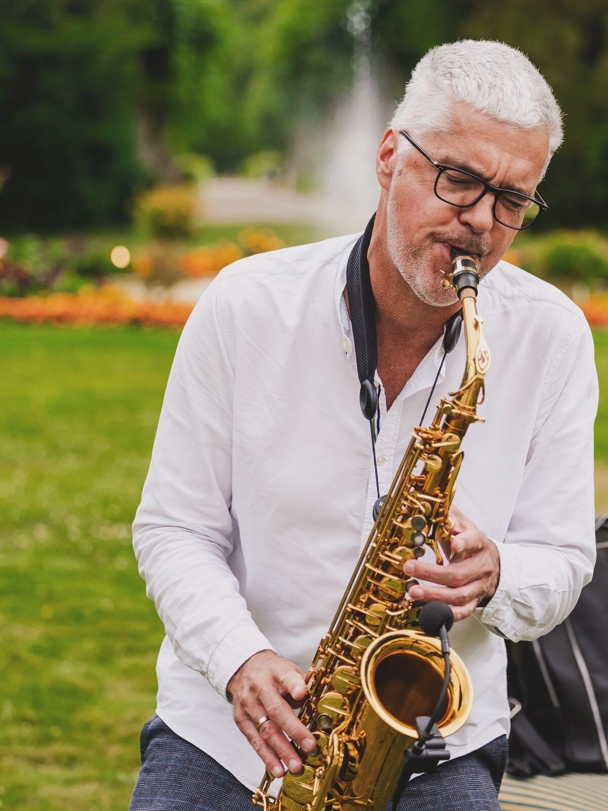 Bert Gerhardt spielt Saxophon im Freien, im Hintergrund ein Park mit Springbrunnen